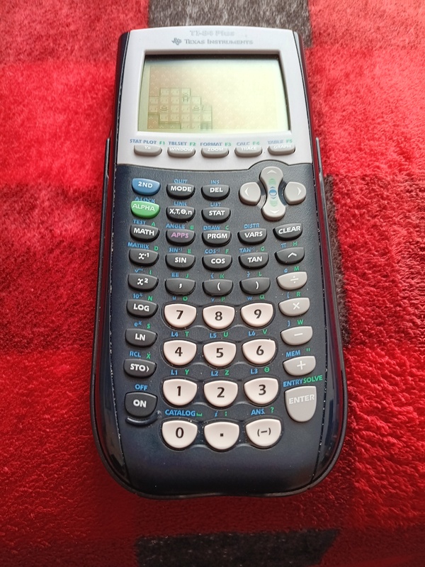 A photograph of my TI-84+, sitting on a red checkered blanked. MExp is running on the calculator.